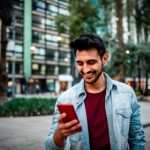 Portrait of a handsome smiling man using mobile phone at the street.